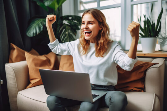 Beautiful young scandinavian woman smiling and rejoices after success. Happy woman celebrating business success on sofa in living room with computer.