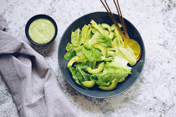 Healthy green salad with fresh vegetables - avocado and lettuce salad leaves on a black plate.