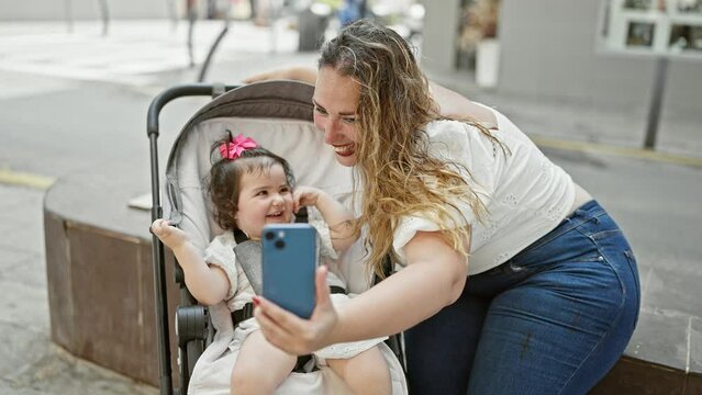 Mum and daughter making confident, smiling selfie with smartphone on city street, enjoying casual, fun family time outdoors