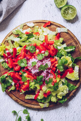 Healthy salad with fresh vegetables - salad romaine, red bell pepper, coriander and red onion on a wooden board