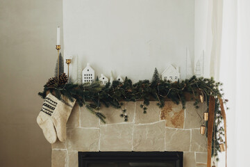 Rustic christmas fireplace with warm knitted stockings and stylish decoration on fir branches. Cozy stockings hanging on mantel in modern farmhouse living room. Atmospheric winter holiday
