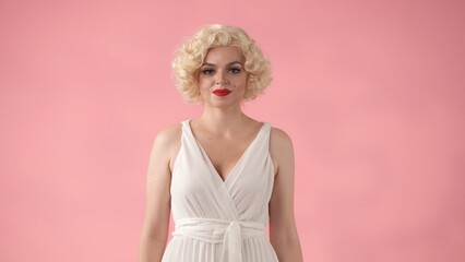 Portrait young woman in wig, white dress and with red lipstick on lips in studio on pink...
