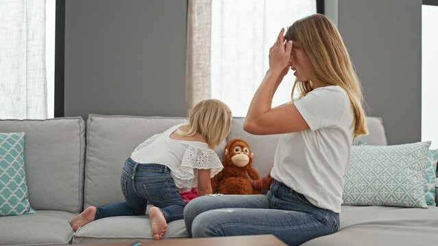 Confident caucasian mother and daughter bonding over giggles while jumping on sofa, radiating joy at their relaxing home