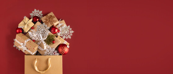 Paper shopping bag full of Christmas gift boxes and balls on a red background with copy space top view. Holiday sale concept