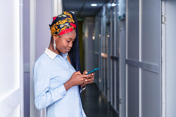 Beautiful young black woman standing in a hallway looking at her cell phone