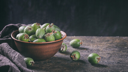 Tropical fruits green ripe feijoa sellowiana berries in a clay bowl and on a table on a dark background. Kitchen banner with copy space for text
