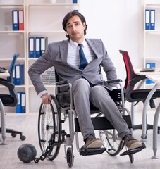 Fototapeta na wymiar Young handsome employee in wheelchair working in the office