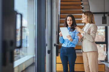 Shot of two young woman working together on digital tablet. Creative female executives meeting in a office using tablet pc and smiling. Two businesswomen holding digital tablet