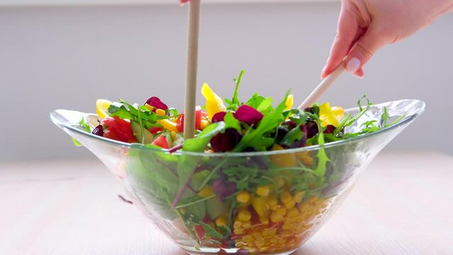 wooden spoons stir salad in glass plate corn tomatoes cucumbers bulgarian yellow peppers arugula leaves vegetarian food lunch slimming diet close-up female hands