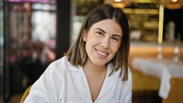 Young beautiful hispanic woman smiling happy sitting on the table at the restaurant