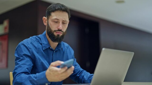 Young hispanic man business worker working looking smartphone and watch at the office