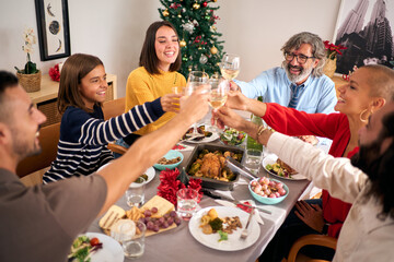 Cheerful European people toasting with white wine at Christmas gathering. Smiling Caucasian family celebrating Christmas vacations together at festive table. Generations enjoying domestic life.