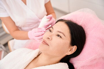 Fototapeta na wymiar Female cosmetologist applies cream to the clients face