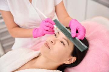 Obraz na płótnie Canvas Esthetician marks the clients eyebrows before the procedure