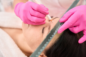 Cosmetologist marks the clients eyebrows before the procedure