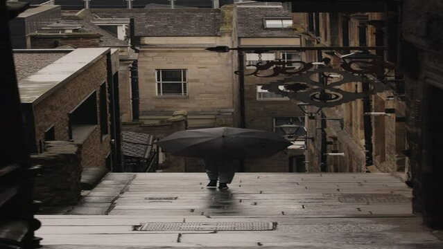 Distant woman carrying umbrella descending wet staircase - vertical / Edinburgh, Scotland