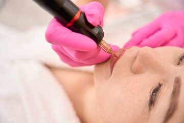 Beauty master in protective gloves applies permanent makeup to client