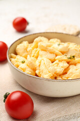 Composition with bowl of scrambled eggs and tomatoes on light background
