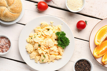 Composition with plate of delicious scrambled eggs with ingredients on white wooden background