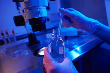 Lab scientist aspirating liquid with Pasteur pipette from reagent bottle