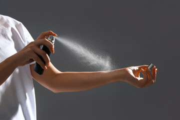 Young woman spraying elegant perfume on grey background, closeup