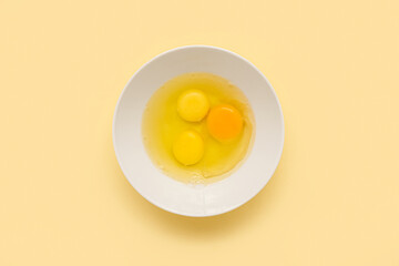 Bowl with cracked chicken eggs on yellow background