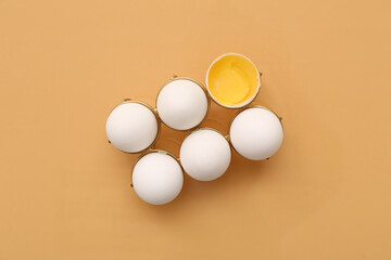 Holder with cracked and whole chicken eggs on beige background