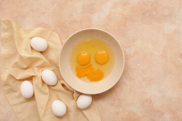 Bowl with cracked chicken eggs on beige background
