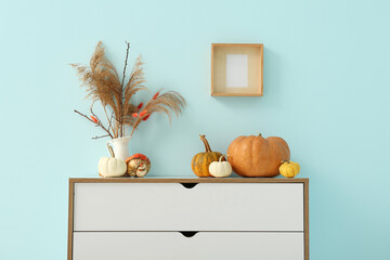 Chest of drawers with pumpkins and pampas grass near blue wall, closeup