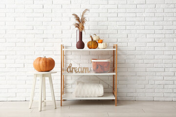 Vase with pampas grass and pumpkins on shelving unit near white brick wall