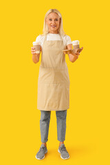 Mature woman with cups of coffee on yellow background