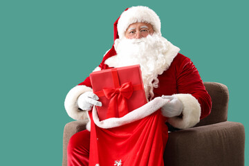 Santa Claus with bag and Christmas gift sitting on armchair against turquoise background