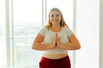 Smiling young woman standing standing on mat yoga looking at camera at home in apartment