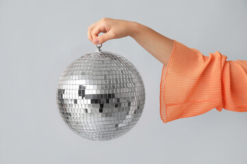 Female hand with disco ball on grey background