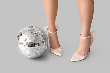 Female legs in stylish high heels with disco ball on grey background