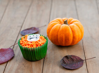 orange cupcakes, pumpkin and autumn leaves for Halloween on wooden background