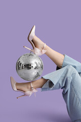Female legs in stylish high heels with disco ball on purple background