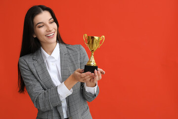 Young businesswoman with gold cup on orange background