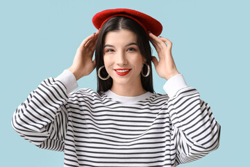 Beautiful young woman in beret with red lipstick on blue background