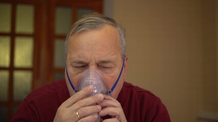 An elderly man puts on an inhaler mask. A man does a respiratory procedure at home. Closeup.