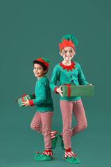 Cute little children in elves costumes with Christmas gift boxes on green background