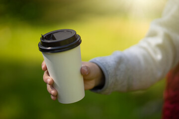 A hand holds out a glass of coffee.Cheer up in the morning.Drink tea in nature.Offer drinks.