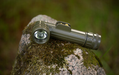 A green military flashlight lies on a granite stone.Equipment for the hike.Lighting at night.