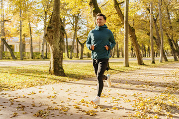 Fototapeta premium A man in warm sports clothes and thermal underwear runs fast in the autumn park. Athlete training every day and in winter. Beautiful bright autumn colors.