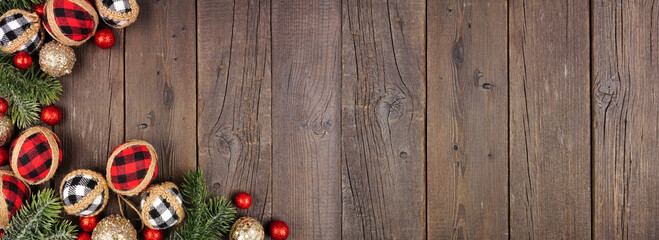 Christmas corner border of red, black and white gingham ornaments, branches and baubles. Overhead view on a dark wood banner background. Copy space.