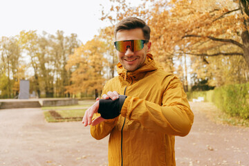 Portrait of a happy person Motivation for an active lifestyle on an autumn day. A male running coach uses a smart watch and a fitness app. In sports glasses for running, smiling.