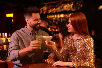 Happy couple clinking glasses with fresh cocktails at table in bar