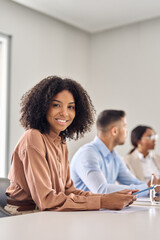 Vertical portrait of happy young African American business woman at diverse team office meeting. Smiling professional businesswoman company employee leader with tablet sitting in board room.