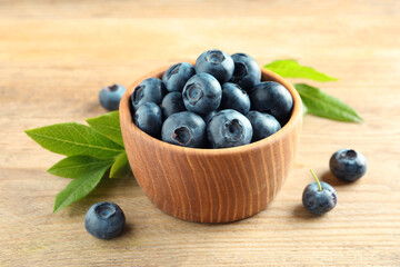 Bowl of fresh tasty blueberries and leaves on wooden table, closeup