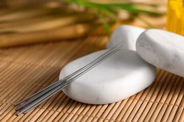 Acupuncture needles and spa stones on bamboo mat, closeup